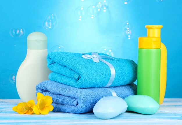 Baby cosmetics towels and soap on wooden table on blue background