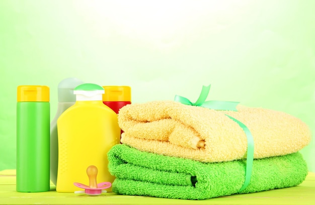 Baby cosmetics and towels on wooden table on green background