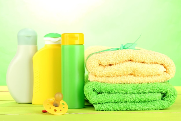 Baby cosmetics and towels on wooden table on green background