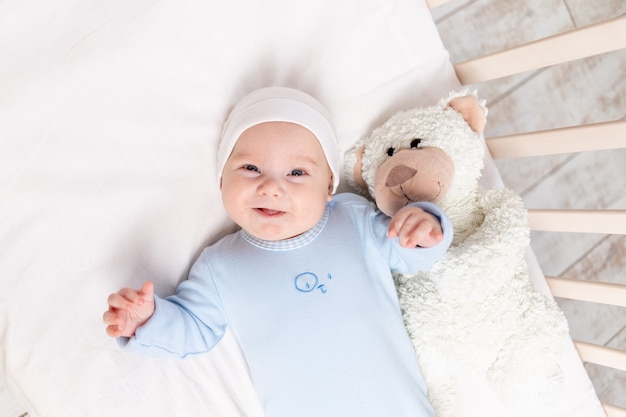 Baby in the crib, portrait of a smiling baby 3 months in the crib with a teddy bear toy, children and birth concept