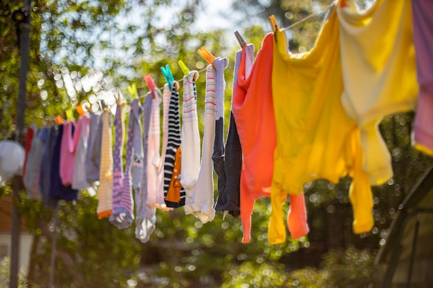 Baby cute clothes hanging on the clothesline outdoor. Child laundry hanging on line in garden on green background. Baby accessories.