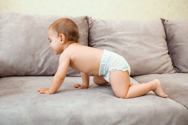 Baby in a diaper crawls on the couch. baby is 11 months old.