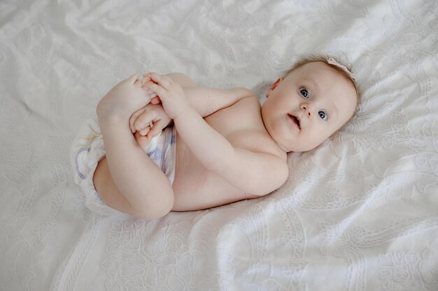 A baby in a diaper is laying on a bed with a white lace tablecloth.