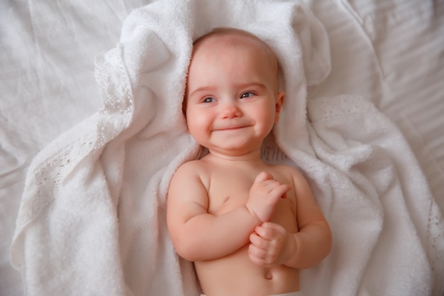 Baby in a diaper is lying in the bedroom on the bed smiling