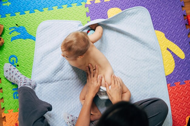 기저귀에 아기가 바닥에 깔린 색깔의 양탄자 위에 파란색 담요 위에 누워 있습니다.