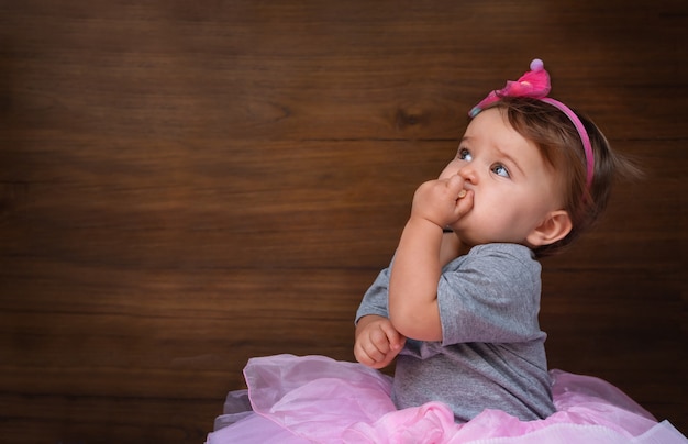 Baby die een koekje op een houten achtergrond eet. Kind in roze jurk op hout achtergrond