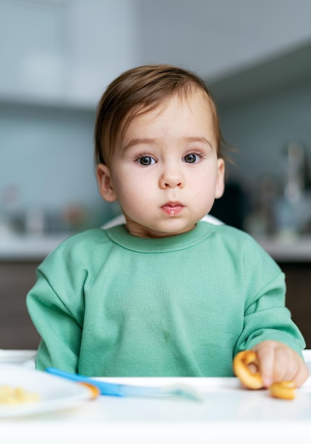 Baby die voedsel op keuken eet Aanbiddelijke babyjongen die koekjes eet die in kinderstoel zitten