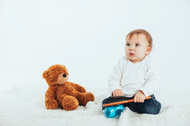 Baby die zijn haar kamt met een teddybeer aan zijn zijde