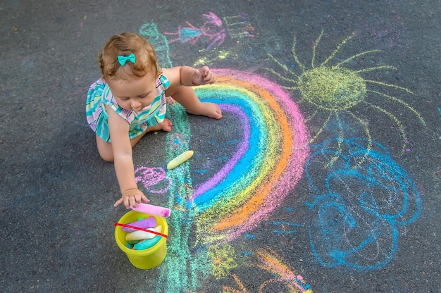 Baby draws a rainbow on the pavement with chalk. Selective focus. Nature.