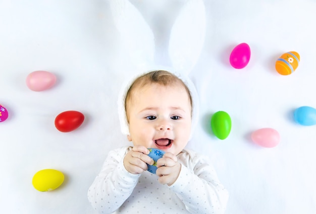 Baby dressed like a bunny with Easter eggs for Easter holiday on white surface