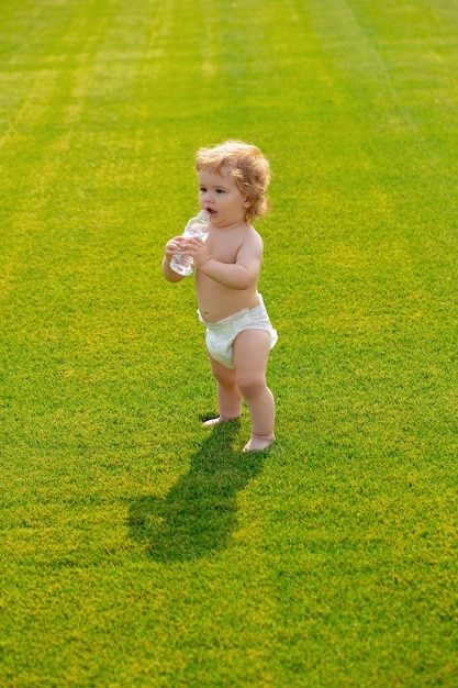 Baby drinking clean water from bottle outdoor on spring green field Healthy child