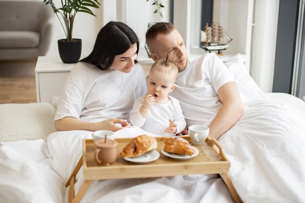 Baby drinking from sippy cup while parents snuggling at home