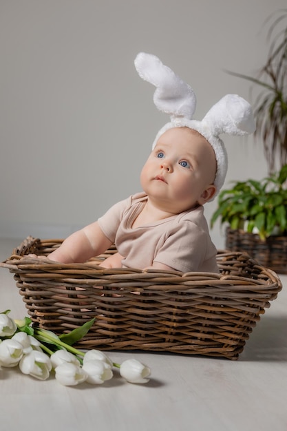 baby in an Easter bunny costume is sitting in a wicker basket on the floor with tulips