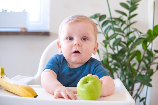 ハイチェアに座ってリンゴを食べる赤ちゃん