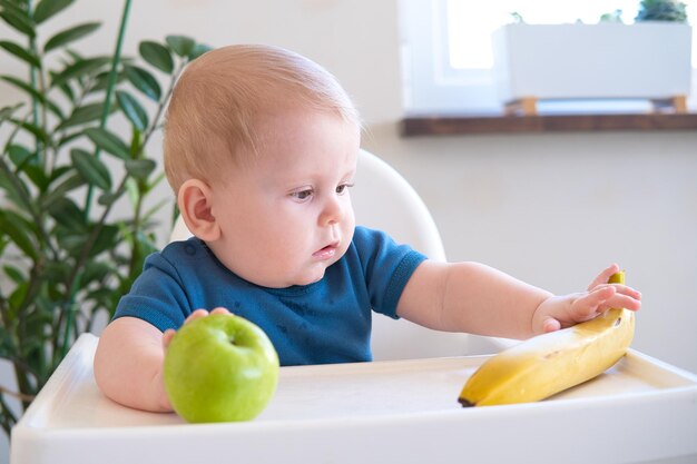 ハイチェアに座ってリンゴを食べる赤ちゃん