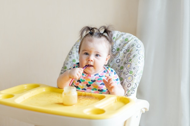 Baby eats himself with a spoon of mashed potatoes from a jar, the concept of baby food