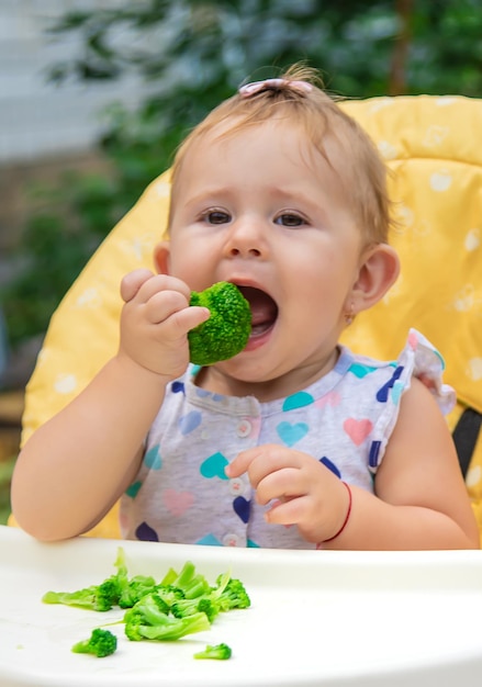 Baby eet stukjes broccoli groenten. Selectieve aandacht. Kind.