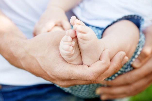 Piedi del bambino nelle mani del padre. piedi minuscoli del bambino sul primo piano maschio delle mani all'aperto. papà e suo figlio. concetto di famiglia felice. bella immagine concettuale della genitorialità.