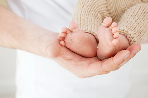 Baby feet in father hands. Tiny Newborn Baby's feet on male hands closeup. Dad and his child. Happy Family concept.