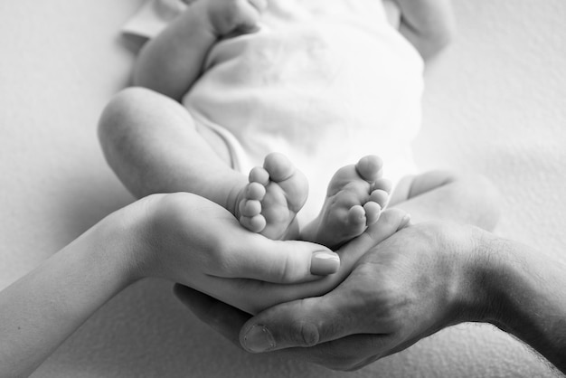 Baby feet in the hands of mother father older brother or sister\
family feet of a tiny newborn close up little children39s feet\
surrounded by the palms of the family black and white