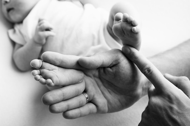 Baby feet in the hands of mother father older brother or sister\
family feet of a tiny newborn close up little children39s feet\
surrounded by the palms of the family black and white