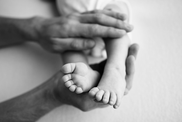 Baby feet in the hands of mother father older brother or sister\
family feet of a tiny newborn close up little children39s feet\
surrounded by the palms of the family black and white