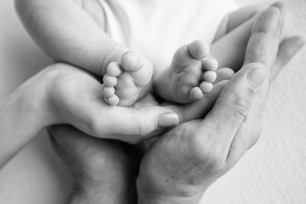 어머니 아버지 형 또는 자매 가족의 손에 있는 아기 발 작은 신생아의 발이 닫힙니다 어린 아이들의 발은 가족의 손바닥으로 둘러싸여 있습니다 흑백