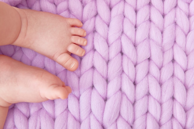 Детские ножки на большом вязаном сиреневом одеяле. Открытка для детского душа, родов, беременности. Copyspace.