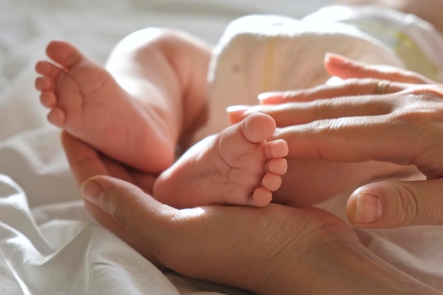 Baby feet in mother hands on her palm Happy parents holding their baby feet close up Maternity family birth concept Woman touching legs of infant baby Tiny foot of newborn Mom and her Child