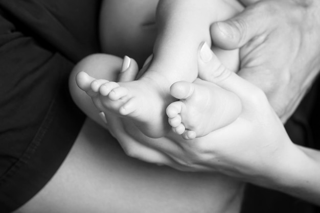 両親の手の中の赤ちゃんの足 両親の形をした手のクローズアップに小さな新生児の赤ちゃんの足