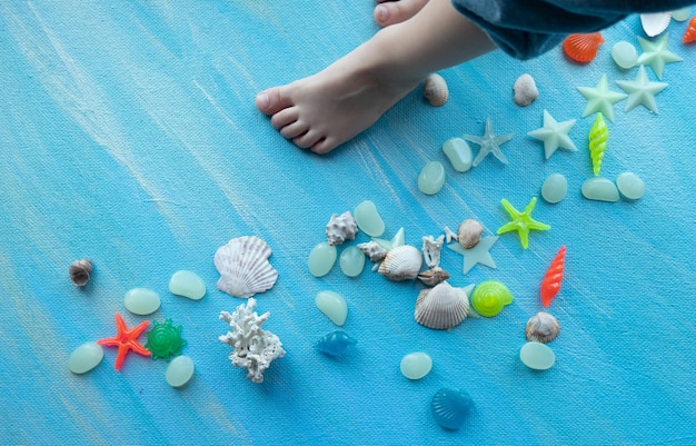 Piedi del bambino su sfondo estate seashells molte diverse stelle marine di conchiglie su uno sfondo di pennellate di vernice blu posto per il testo