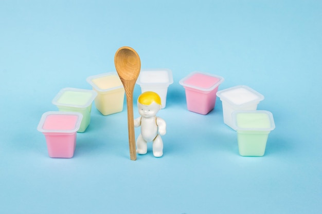 A baby figurine with a wooden spoon and a large number of colorful yogurt cups. Natural healthy food. Fruit and milkshakes.