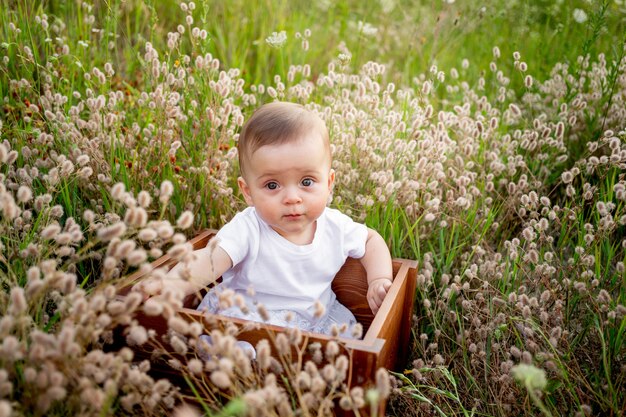 Baby in flowers on the field in summer in a white dress