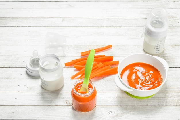 Baby food. Baby carrot puree with milk in a bottle. On a white wooden table.