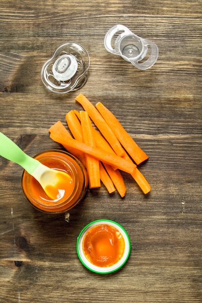 Baby food. Baby puree carrot with a nipple. On a wooden table.