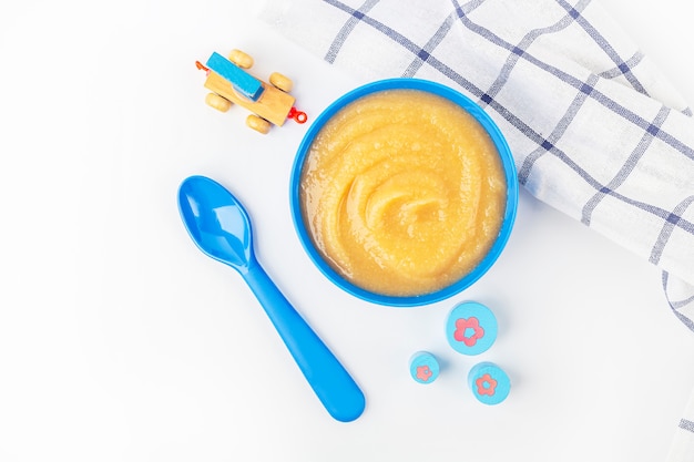 Baby food. Fresh homemade applesauce. Blue bowl with fruit puree on fabric and kids toys on table. The concept of proper nutrition and healthy eating. Organic and vegetarian food. Copy space for text