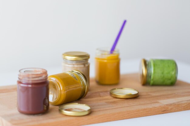 Photo baby food, healthy eating and nutrition concept - vegetable or fruit puree in glass jars and feeding spoon on wooden board