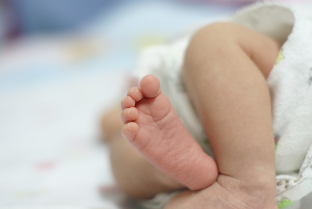 Piede del bambino sul fondo bianco del letto di colore