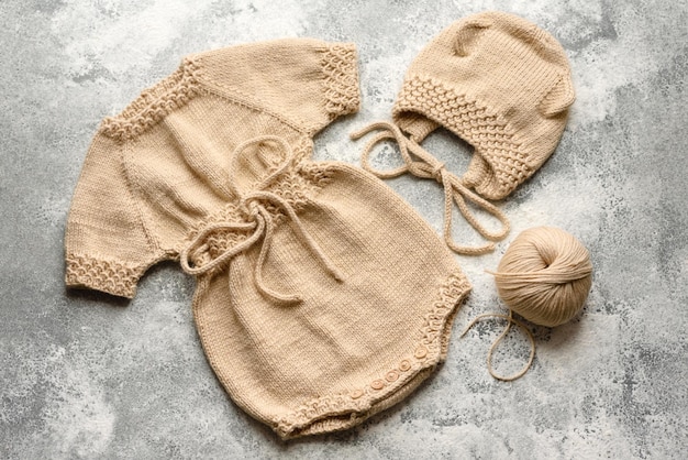 Baby gebreide beige kleren op een witte betonnen achtergrond