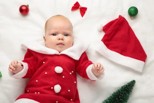 Baby gekleed voor eerste kerst met kerstversiering op witte achtergrond.