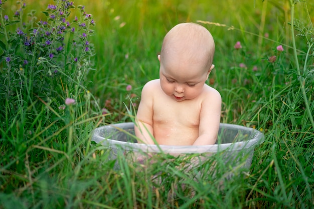 Baby girl 10 months old bathes in a basin in the grass in the summer