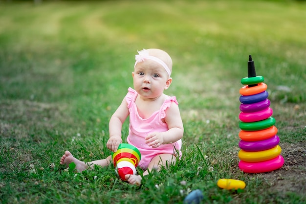 Neonata di 10 mesi seduta sull'erba in estate e giocando a piramide, sviluppo precoce dei bambini, giochi all'aperto