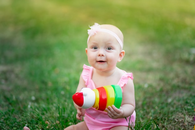 Baby girl 10 months old sitting on the grass in the summer and playing pyramid