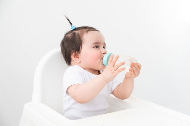 Девочка в детском кресле питьевой водой из детской бутылочки.