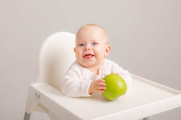 Baby girl in baby chair eating apples on white background Baby first solid food