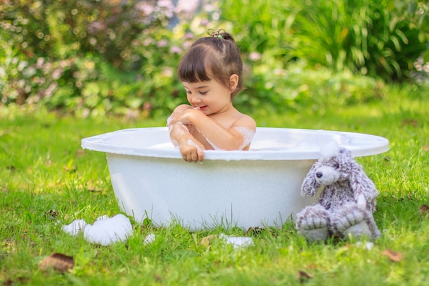 Baby girl bathes in a bathtub in the summer garden