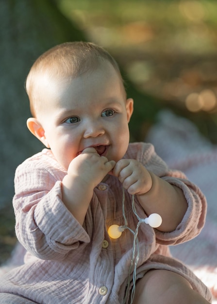 baby girl in a beige dress sitting near a large tree and looking at the camera