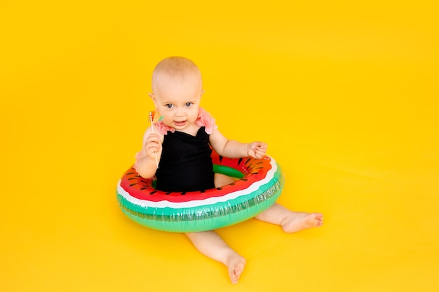 Baby girl in black and pink swimsuit holding watermellon inflatable pool float