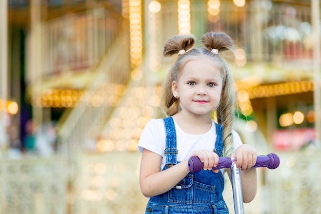 Baby girl blonde riding a scooter in summer at an amusement Park