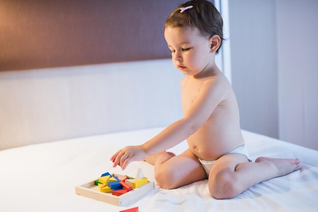 Costruire la bambina con i blocchi bella ragazza carina seduta sul letto in un pasticcio giocattolo che gioca con blocchi di legno colorati da costruzione gioco educativo per bambini in camera da letto creatività della scuola materna